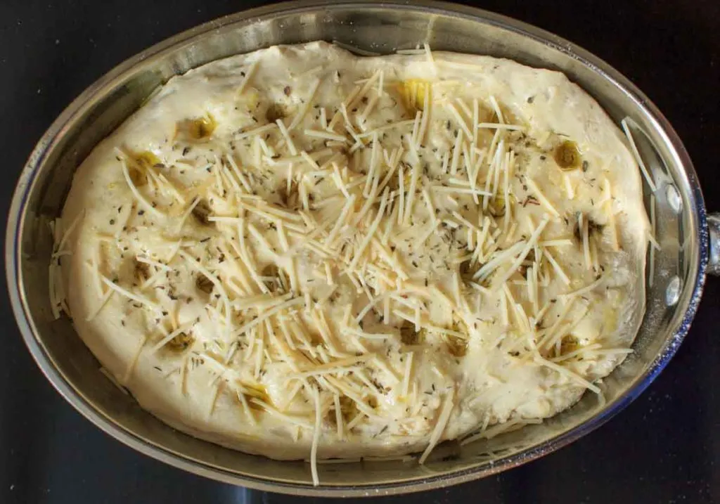 focaccia dough before baking, holes poked and sprinkled parmesan on top