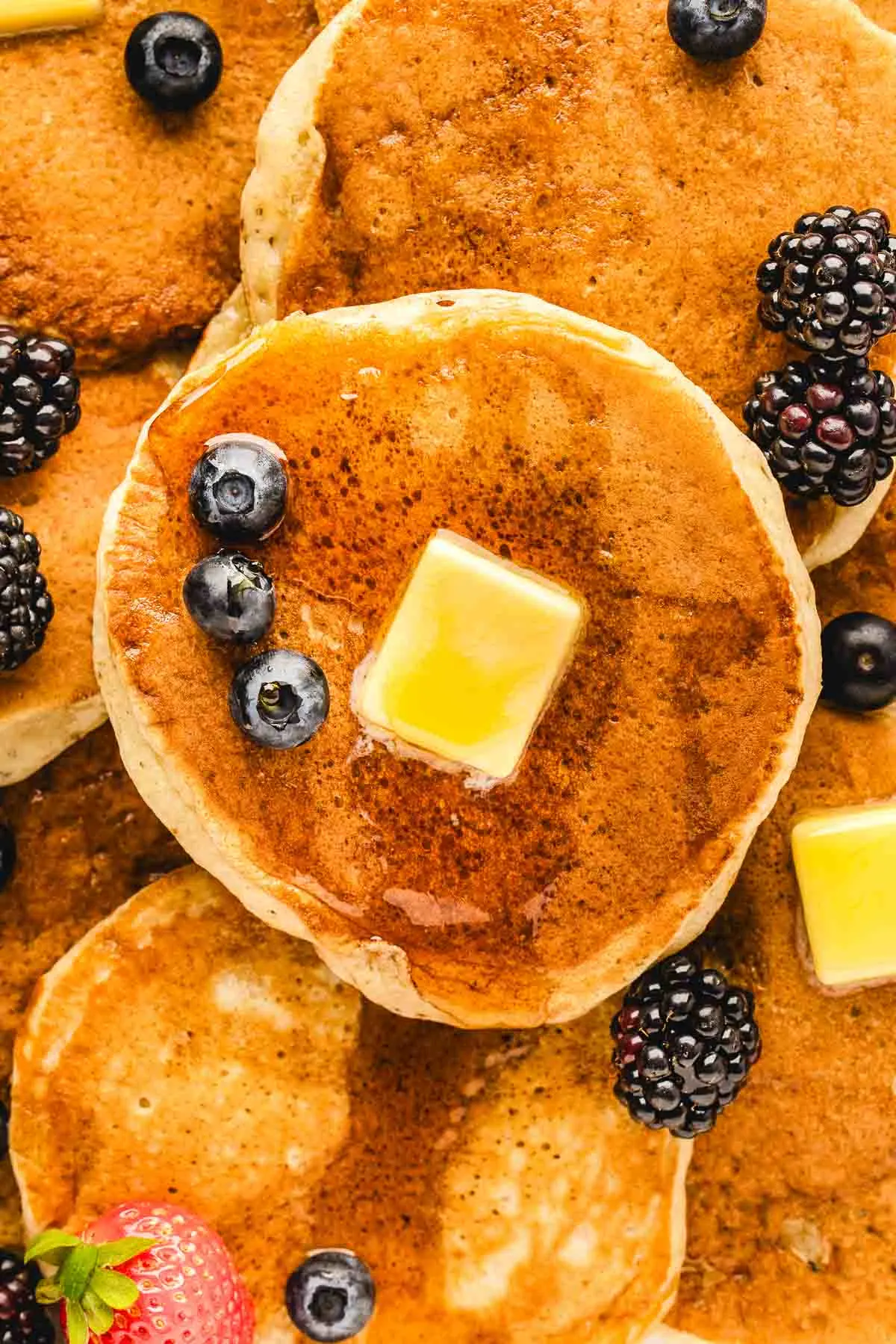 close up of buttermilk pancake stack with fresh berries and globs of butter melting