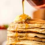 pouring real maple syrup over a big stack of buttermilk pancakes