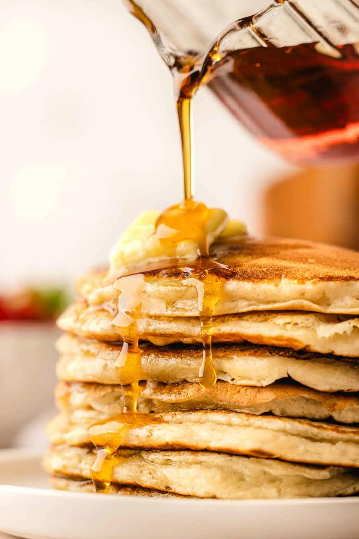 pouring real maple syrup over a big stack of buttermilk pancakes