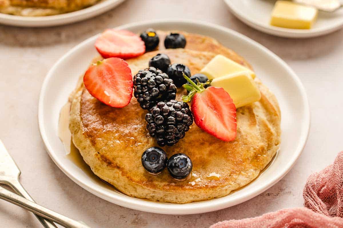 buttermilk pancakes on a white plate with fresh blueberries, blackberries, strawberries, and butter