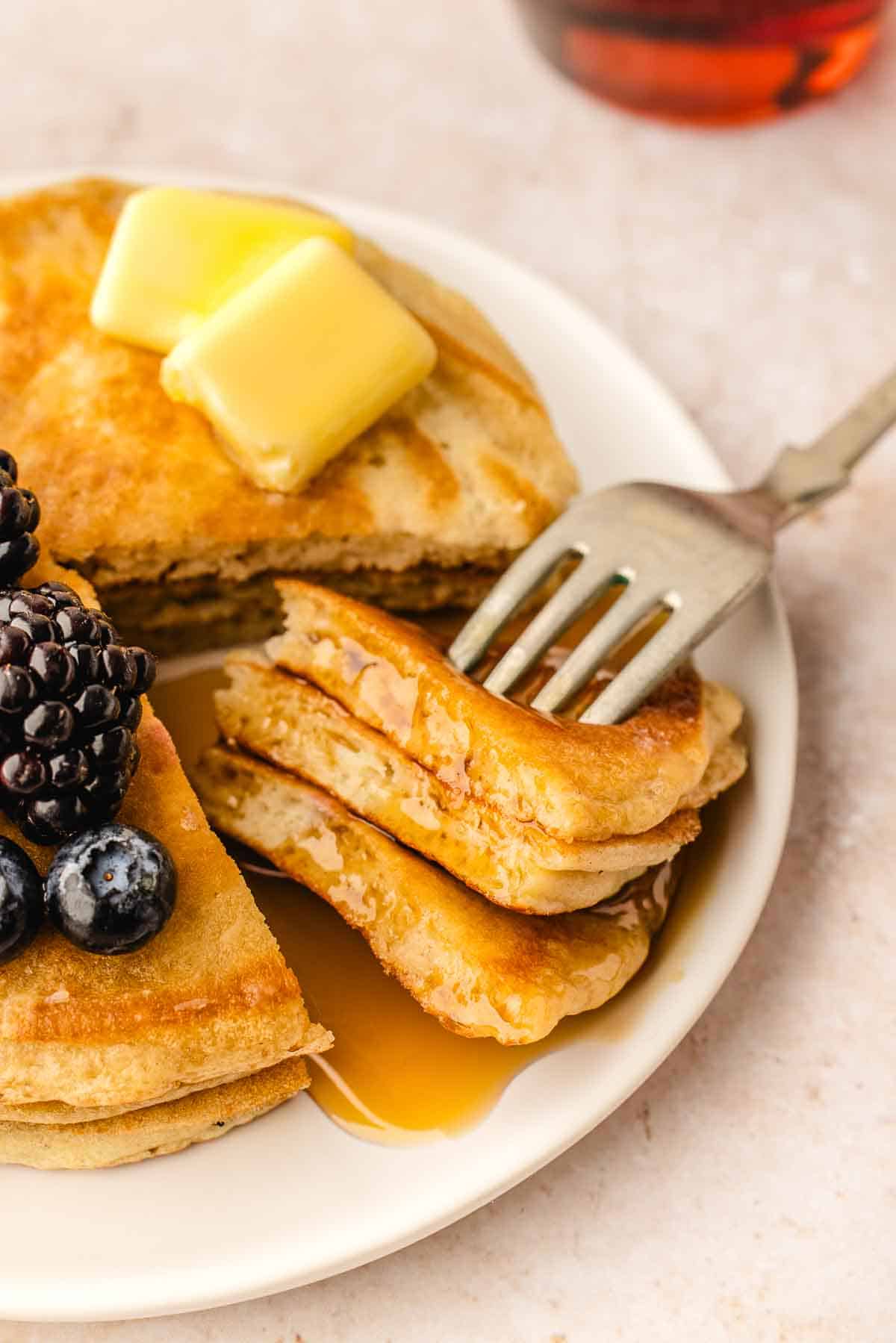 triple layer pancake stack with a wedge cut out of it on a fork bite. Topped with butter chunks and fresh berries on a white plate