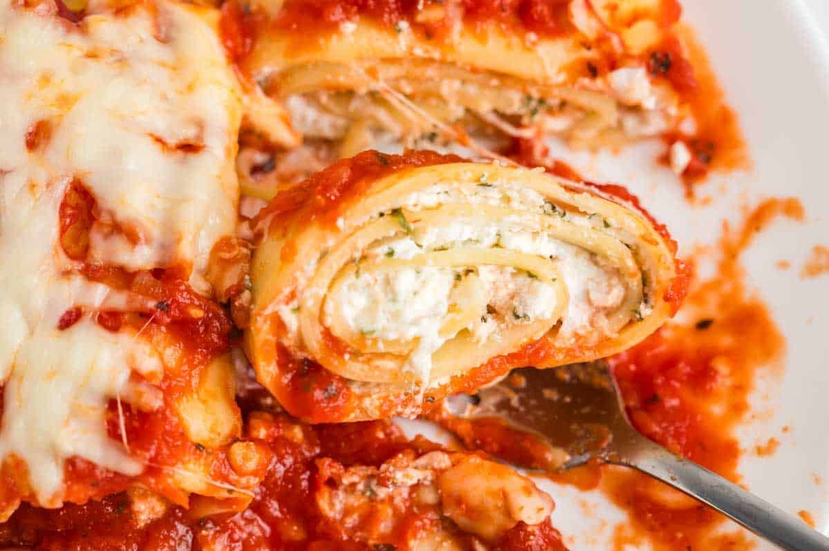 close up of one lasagna roll up from the side pulling up with a fork