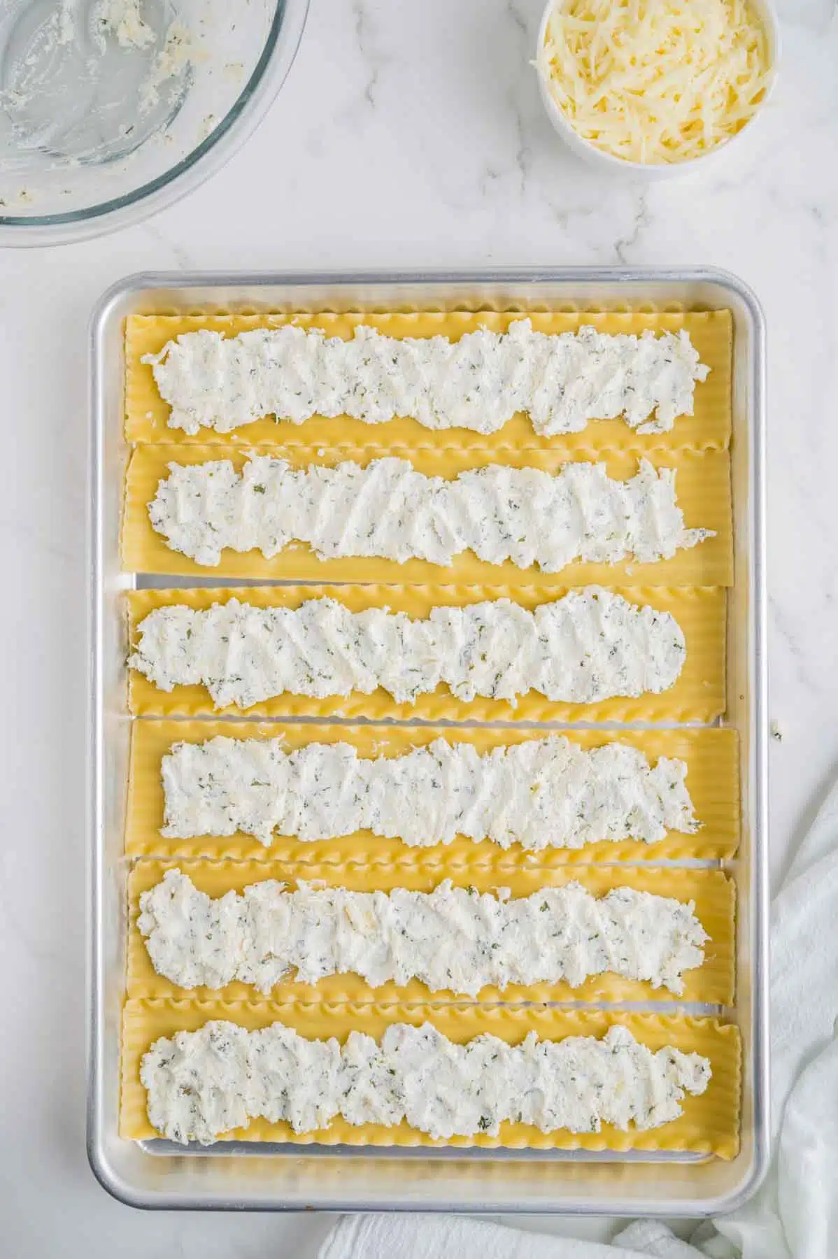 lasagna noodles flat on baking sheet with ricotta cheese mixture spread on top