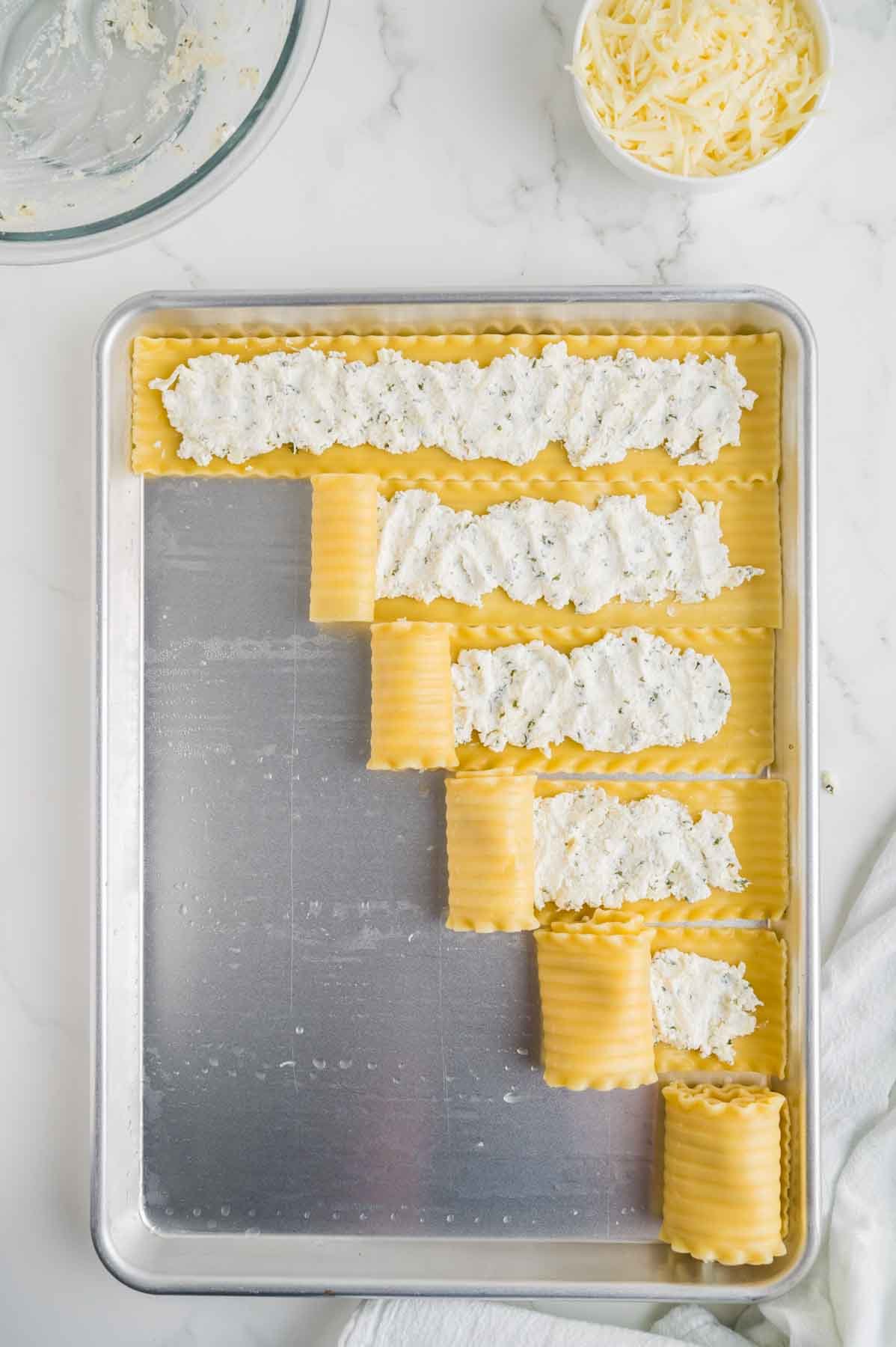 rolling up lasagna noodles and cheese mixture on baking sheet