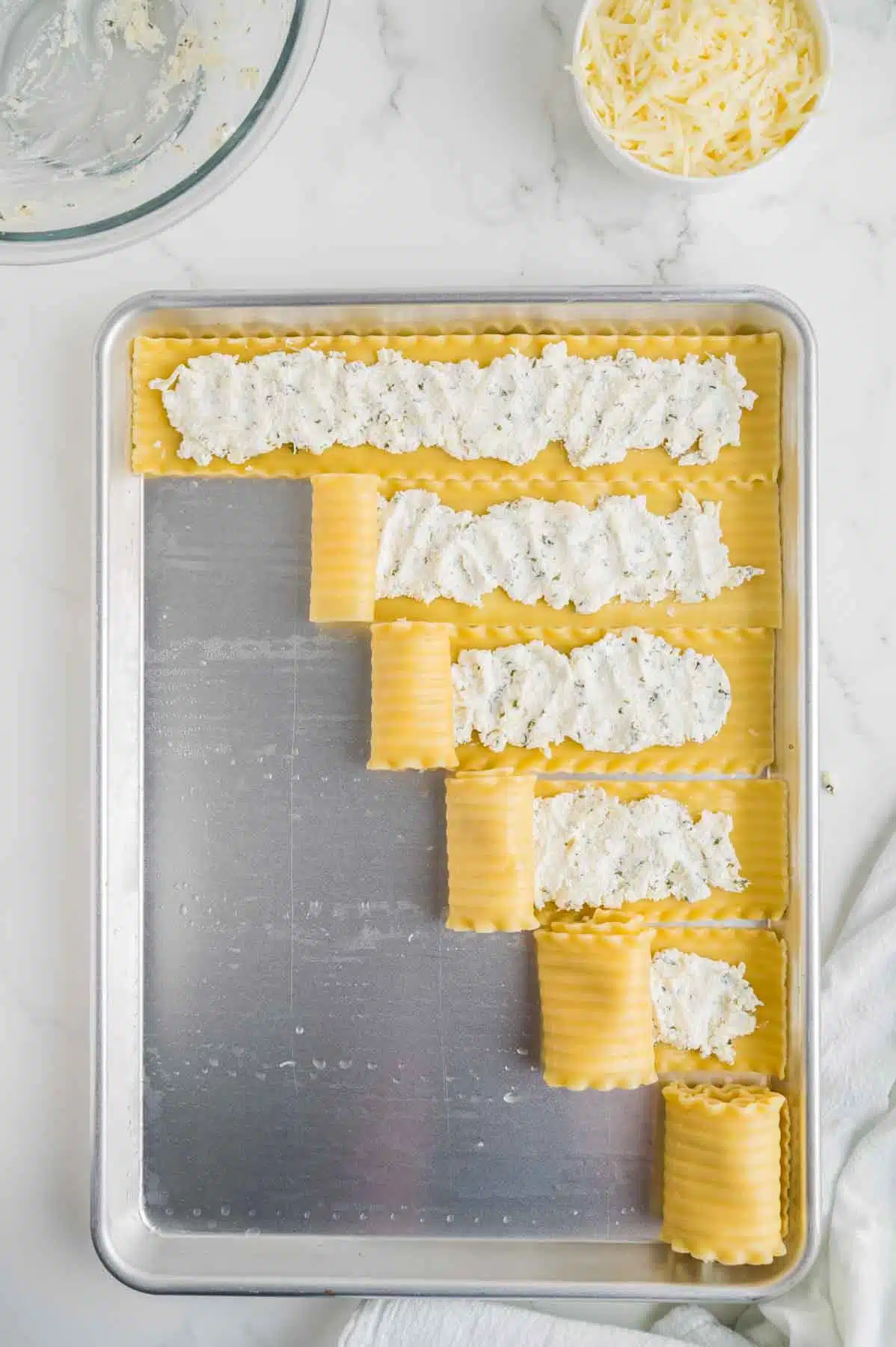 rolling up lasagna noodles and cheese mixture on baking sheet