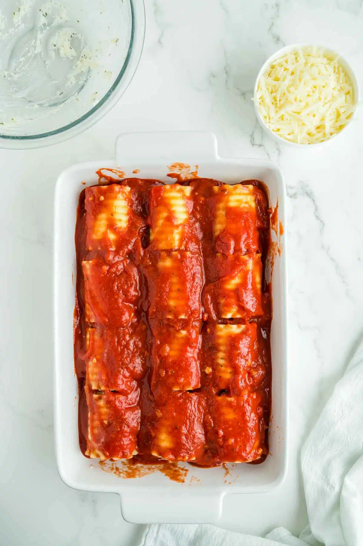 12 lasagna roll ups in a casserole dish with sauce covering before baking