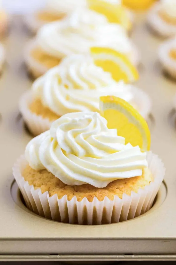 lemon cupcake in cupcake tin with buttercream lemon frosting swirled and a wedge of lemon