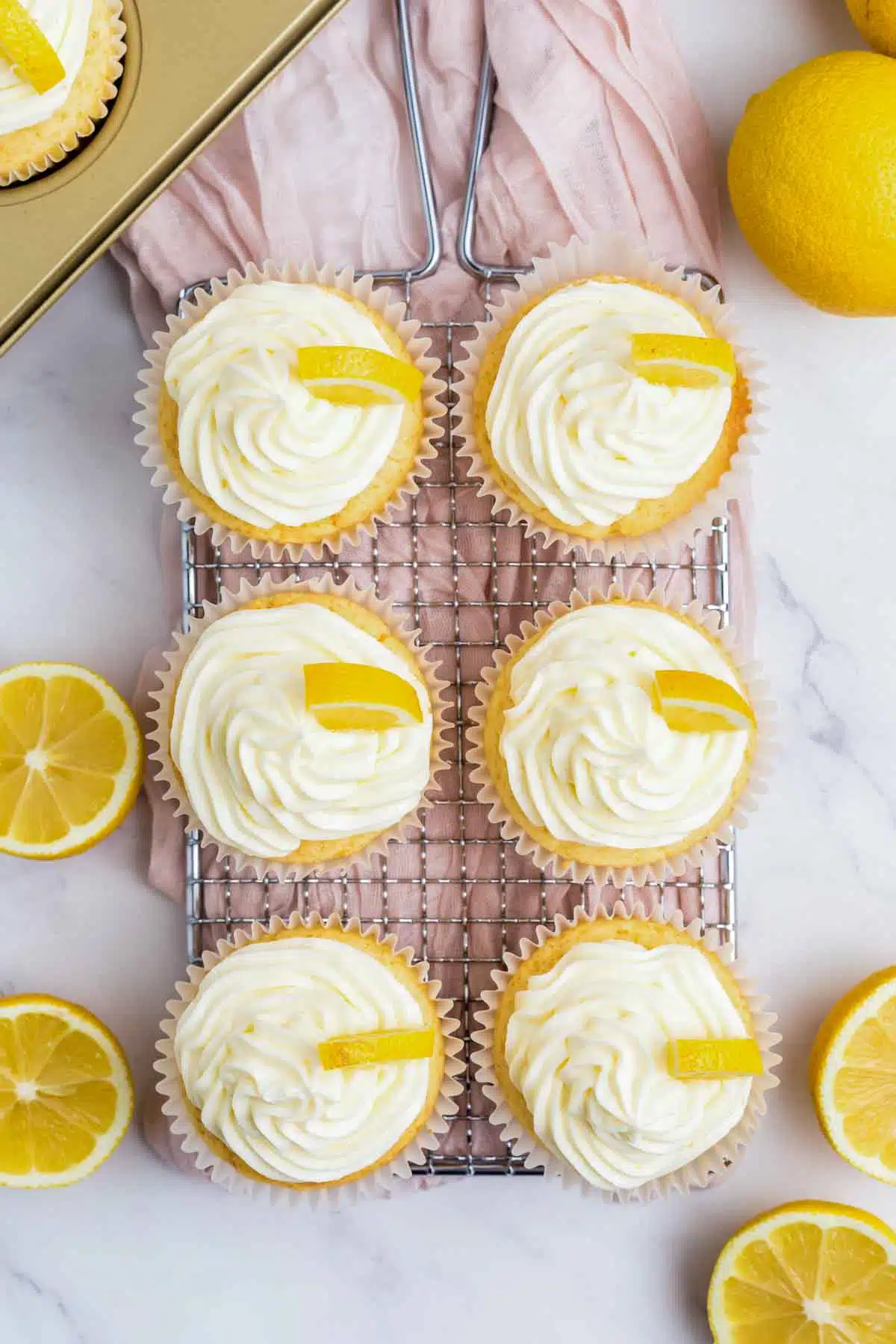 6 lemon cupcakes with frosting and wedges of lemon