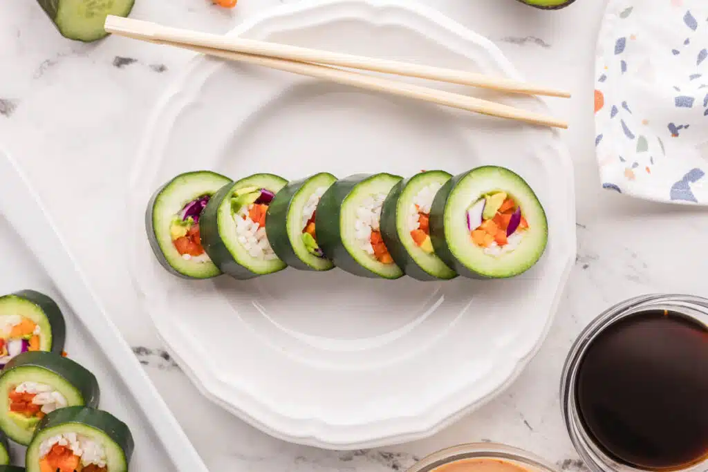 6 cut slices of cucumber sushi on a white plate with chopsticks