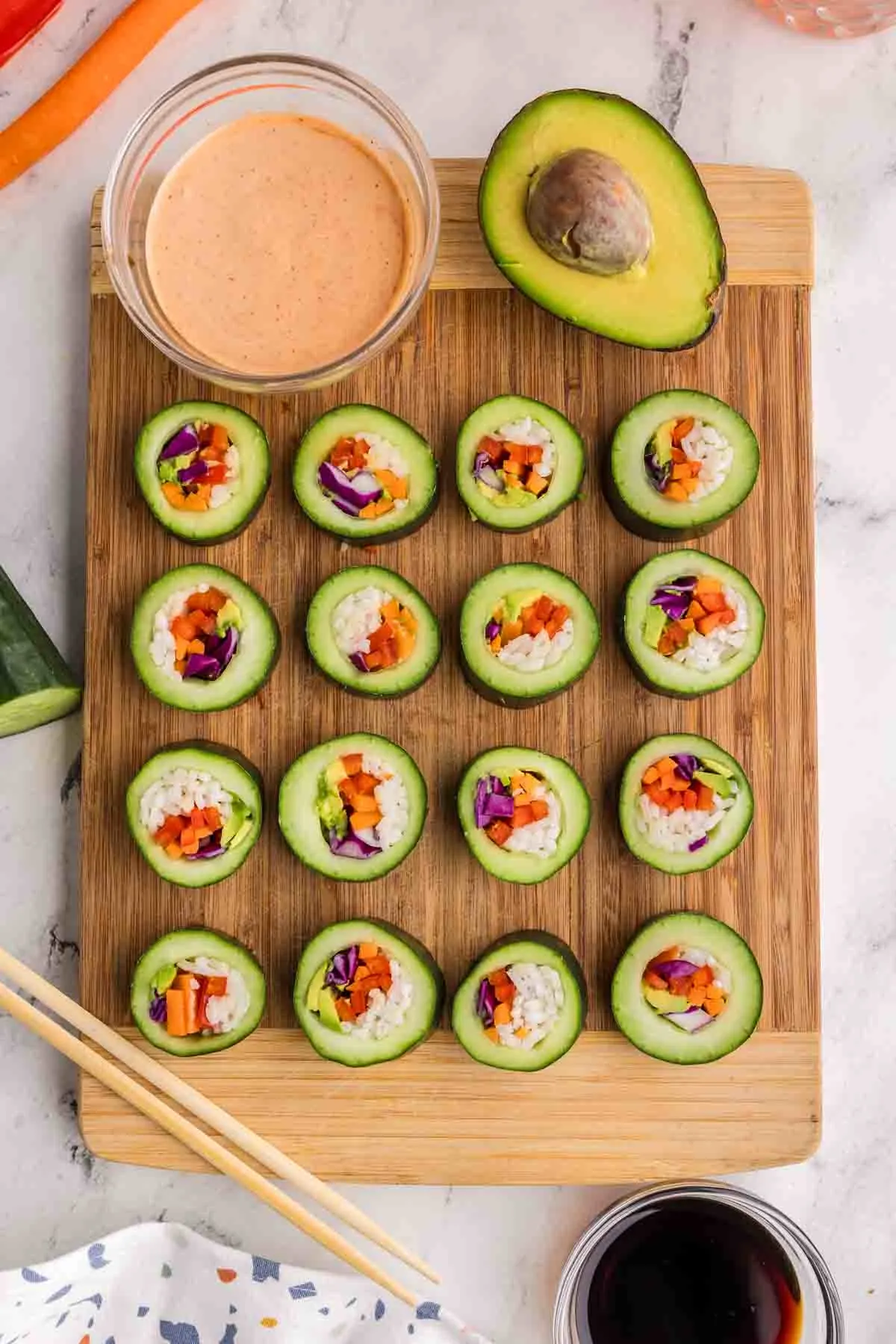 stuffed cucumber veggie sushi on cutting board with dipping sauce and half an avocado