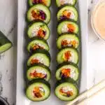 14 prepared pieces of stuffed cucumber sushi on a white serving plate