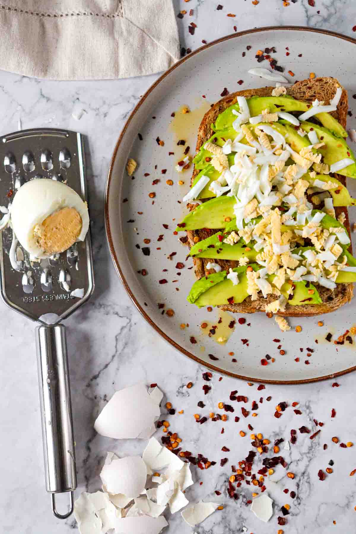 avocado toast with grated egg on top and spices, with half a hard boiled egg and grater next to the plate