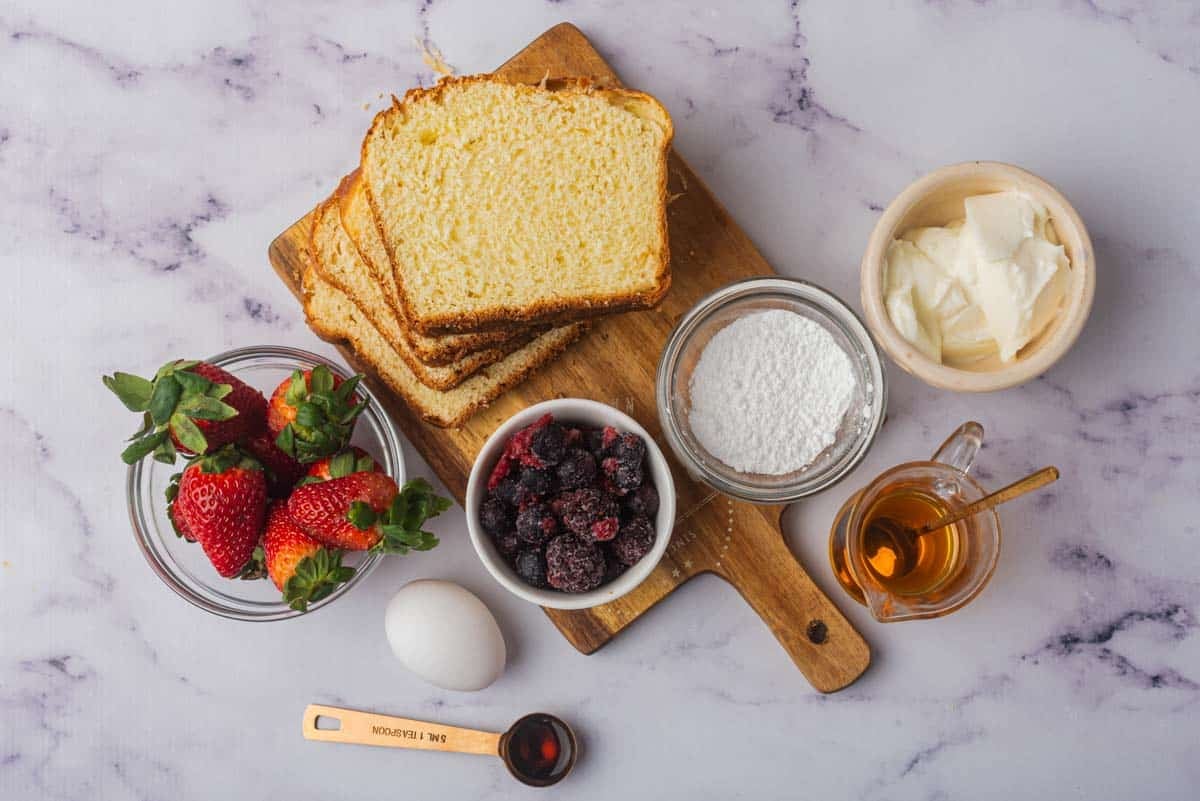 all ingredients needed for yogurt custard toast in individual bowls on counter with wooden cutting board