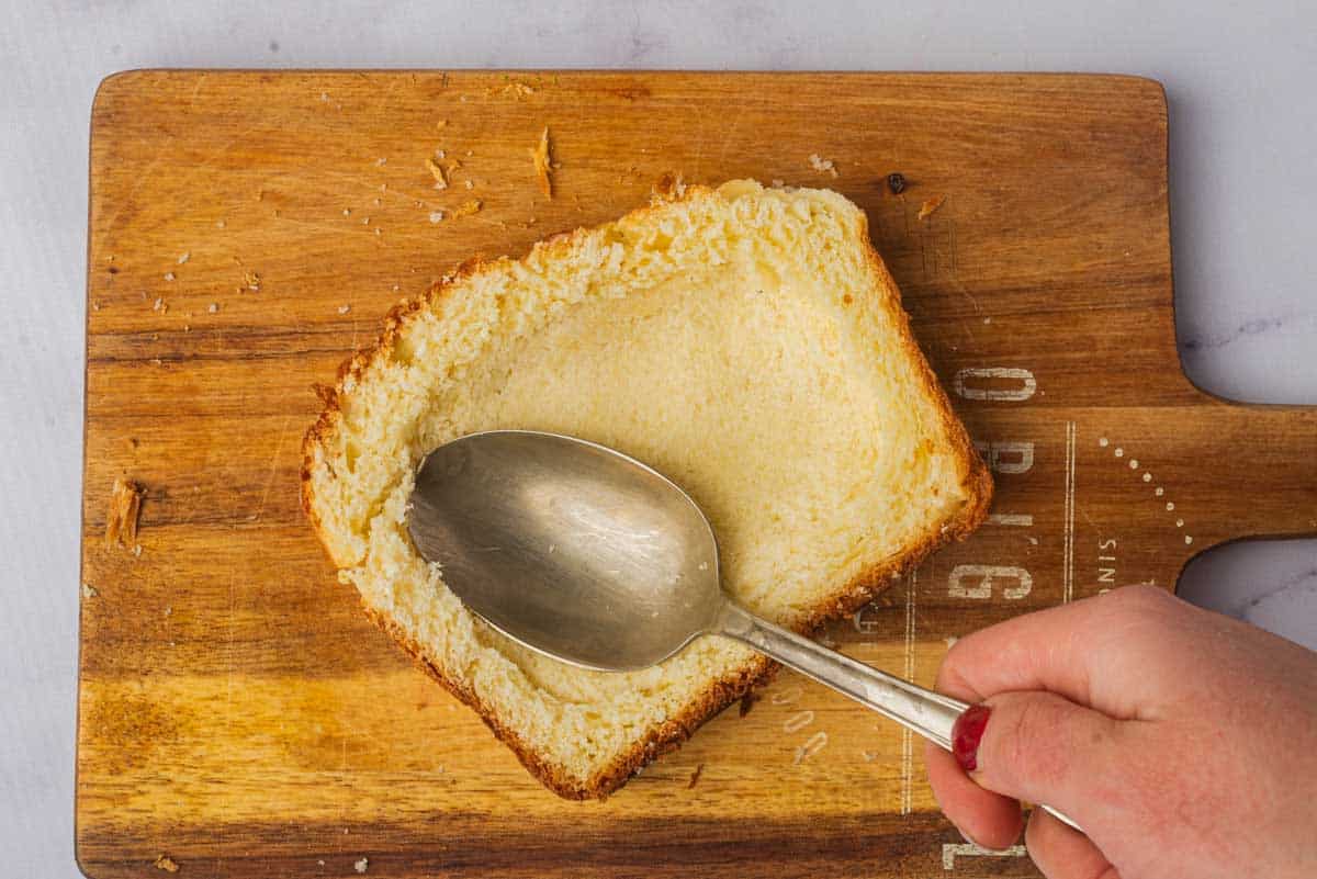 pressing spoon into a piece of bread to make room for the custard