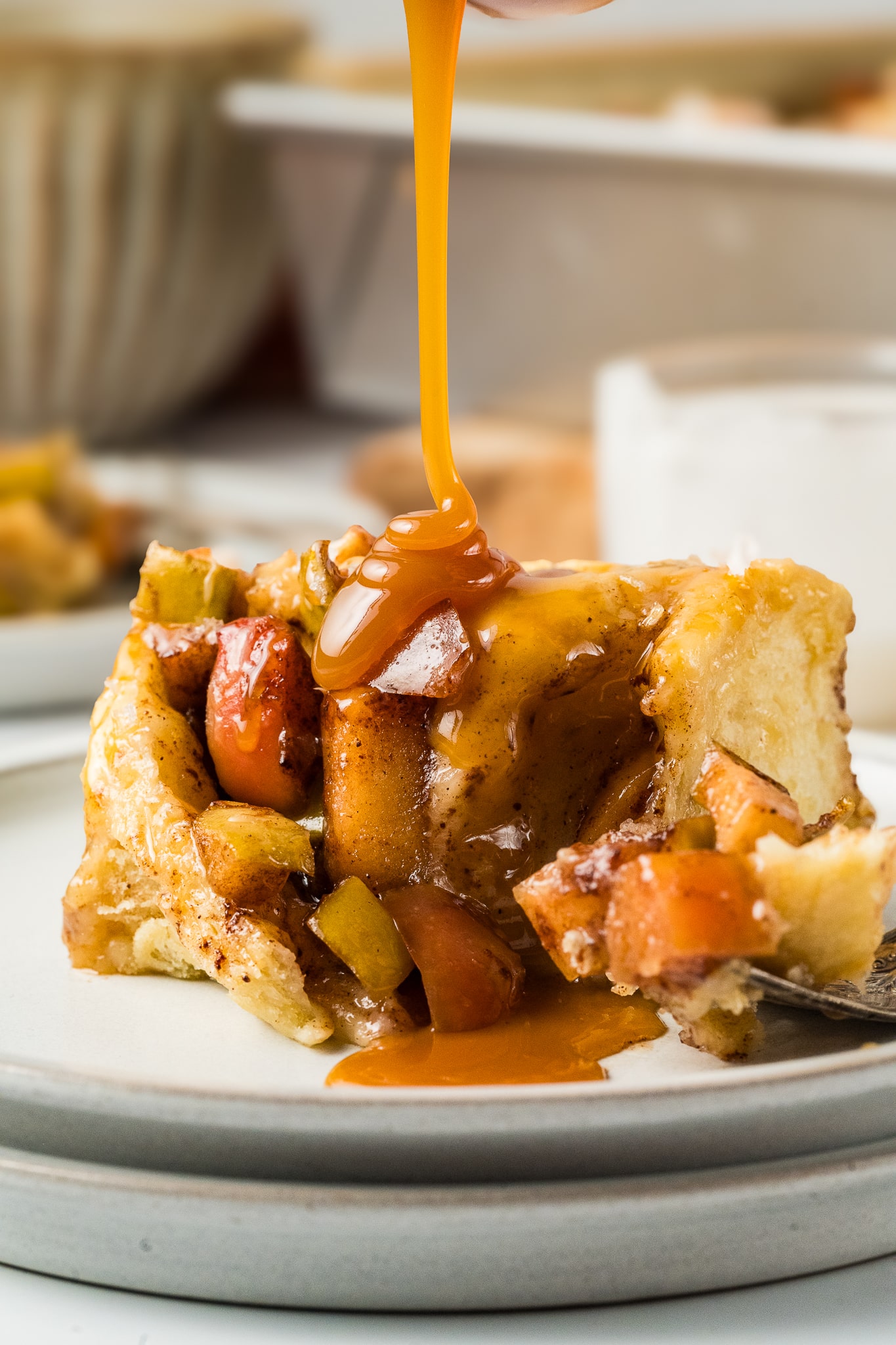 pouring extra caramel sauce over apple cinnamon roll on plate