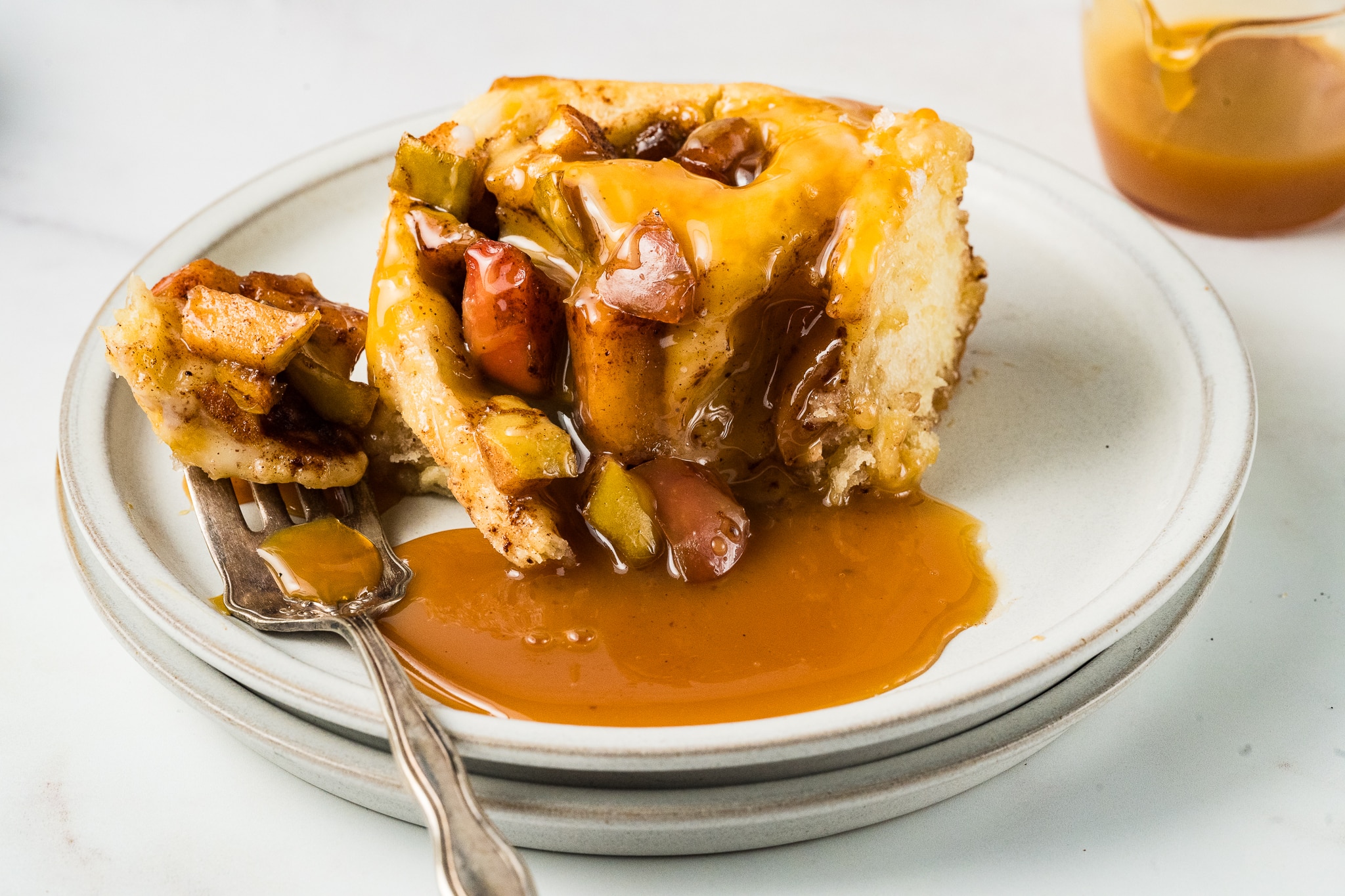 one big caramel apple cinnamon roll with extra caramel and fork on plate