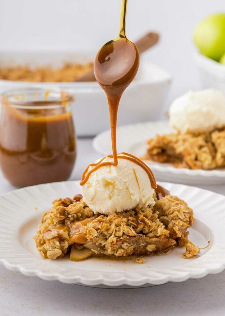 drizzling caramel sauce over top a piece of caramel apple crisp