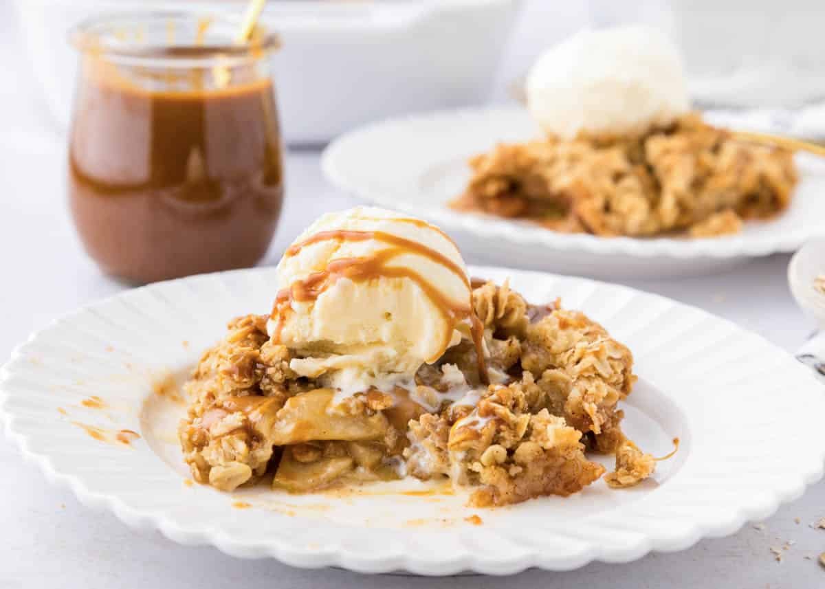 partially eaten piece of caramel apple crisp on white plate topped with a scoop of ice cream and caramel sauce