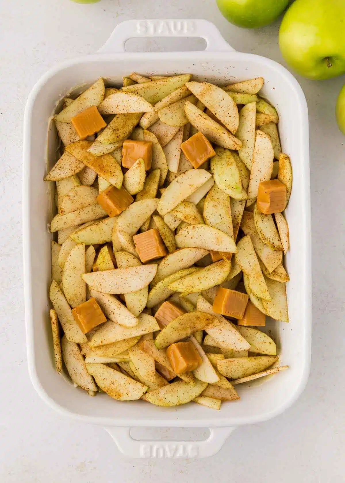 cut up apples in a white casserole dish sprinkled with cinnamon mixture