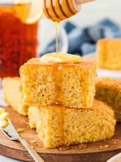 drizzling honey over 2 pieces of gluten-free cornbread on brown serving plate