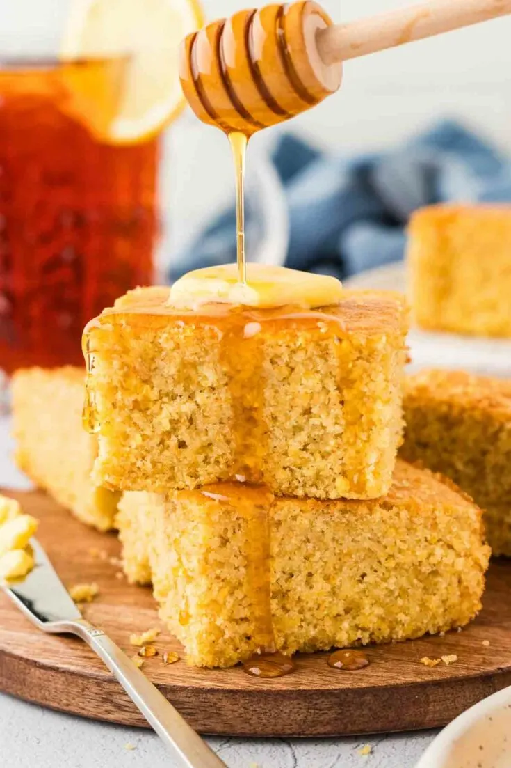 drizzling honey over 2 pieces of gluten-free cornbread on brown serving plate