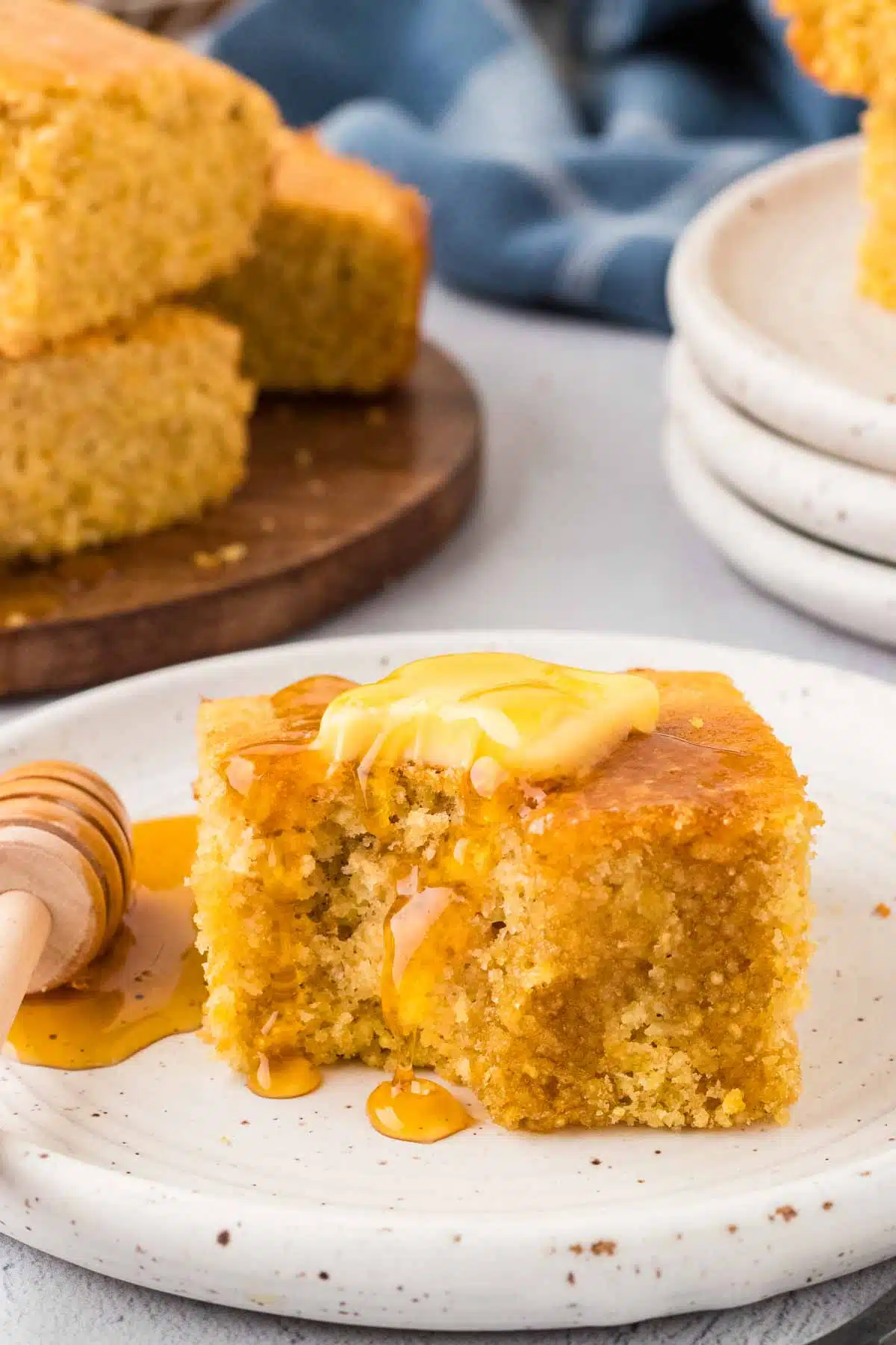 a serving of gluten free cornbread on white plate topped with pad of butter and honey, with a bite taken out