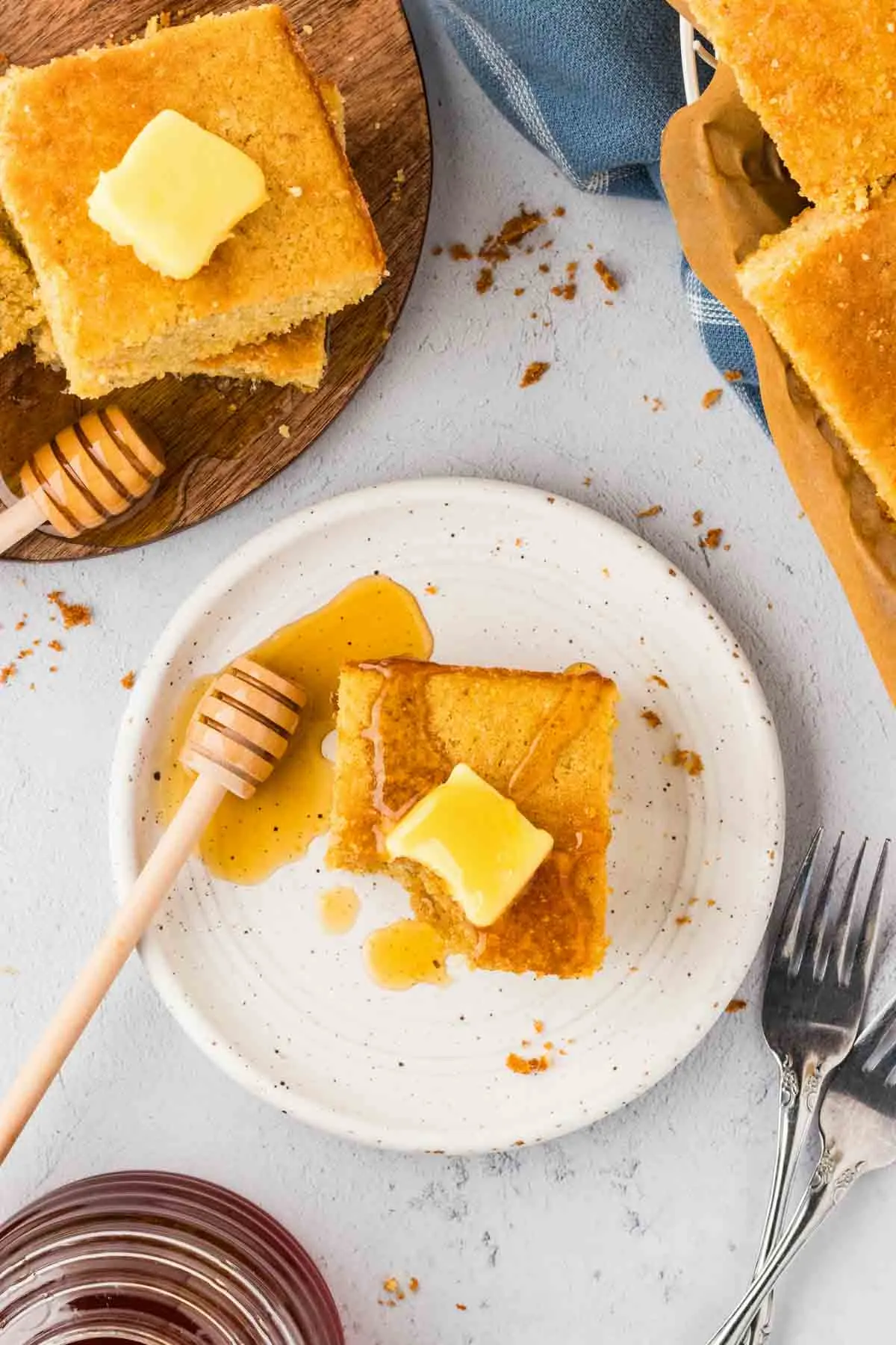 overhead shot of cornbread pieces topped with butter, and a honey stick on white plate