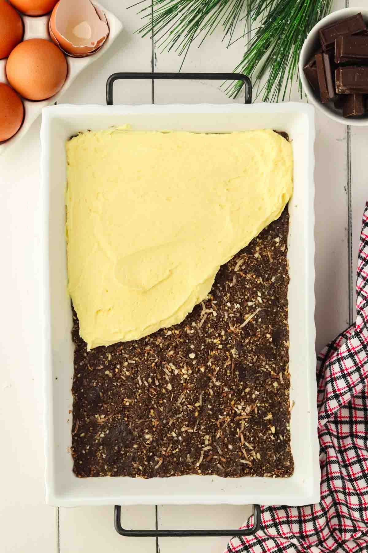 pouring custard over chocolate graham cracker layer in white casserole dish