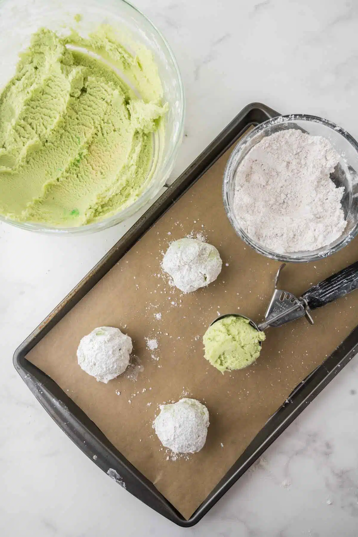 scooping key lime cookie dough on baking sheet with a few covered in powdered sugar