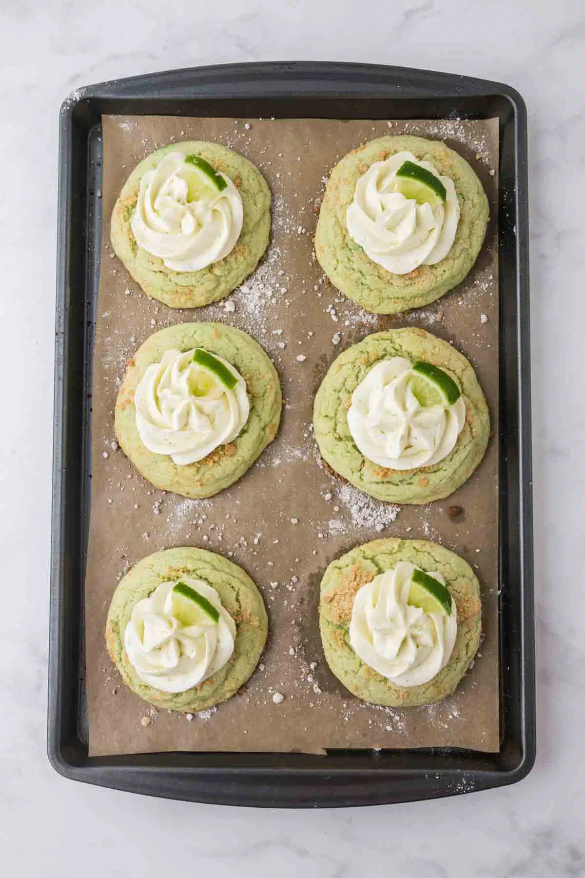 6 large key lime cookies topped cream cheese topping and slices of key lime on baking sheet