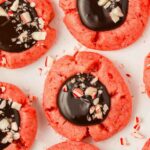 chocolate ganache topped with peppermint bits on a red colored peppermint thumbprint cookie