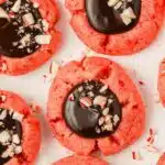 chocolate ganache topped with peppermint bits on a red colored peppermint thumbprint cookie