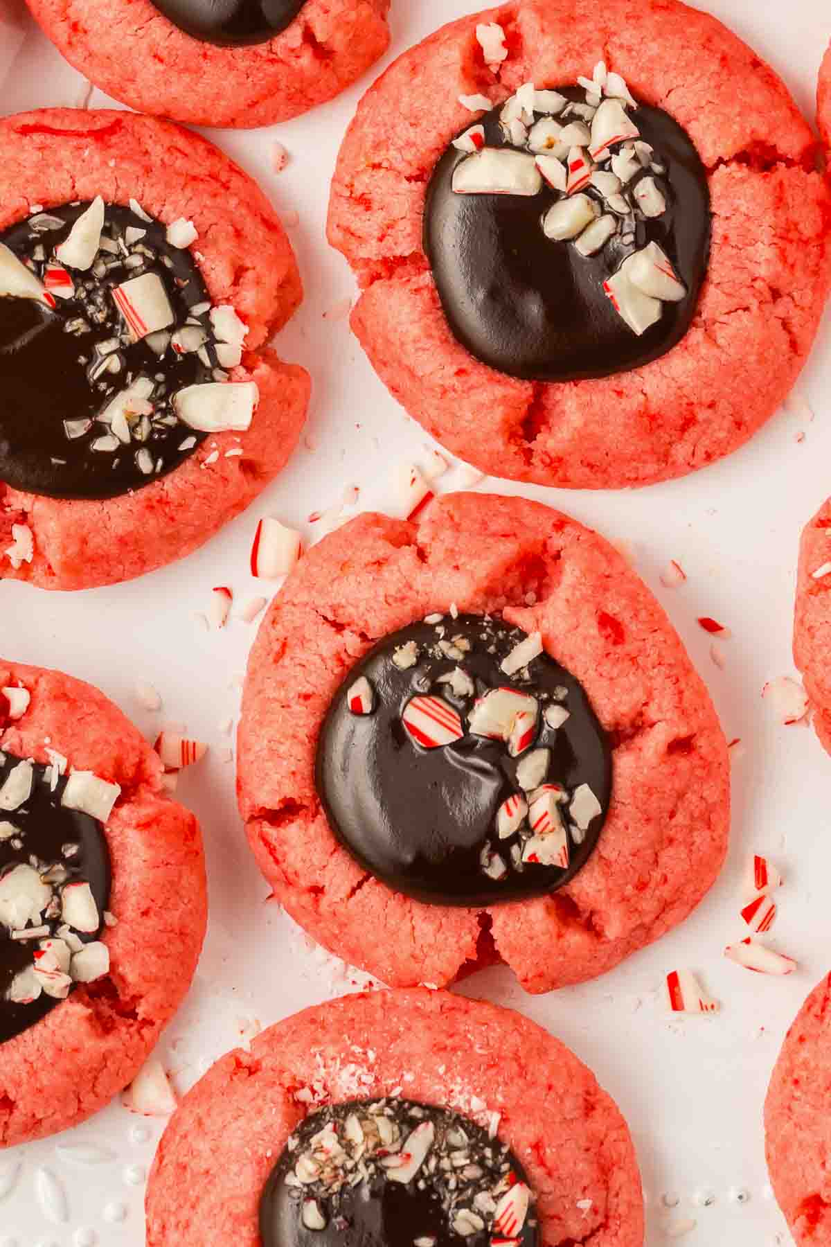 chocolate ganache topped with peppermint bits on a red colored peppermint thumbprint cookie