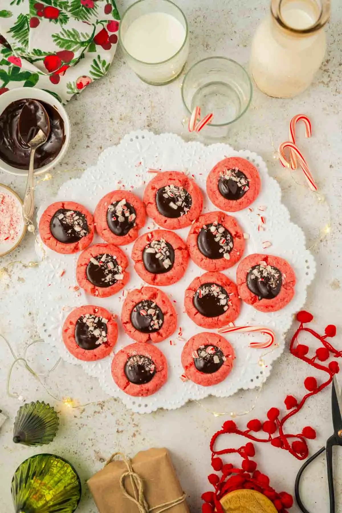 13 peppermint thumbprint cookies with chocolate ganache on a white plate with holiday decorations around it