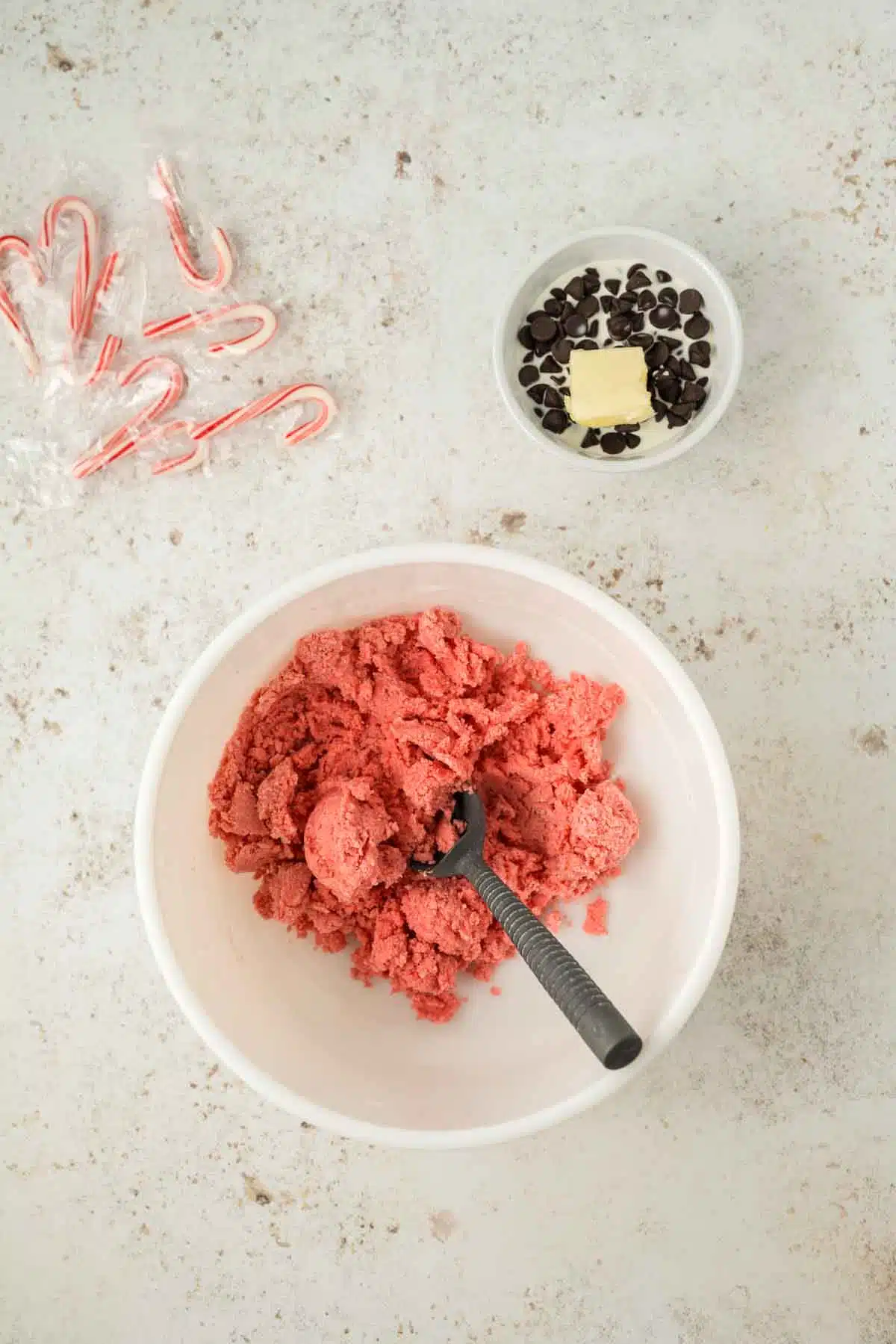 white bowl with peppermint cookie dough with another small bowl filled with chocolate ganache ingredients ready to prepare, and mini candy canes in the corner of picture