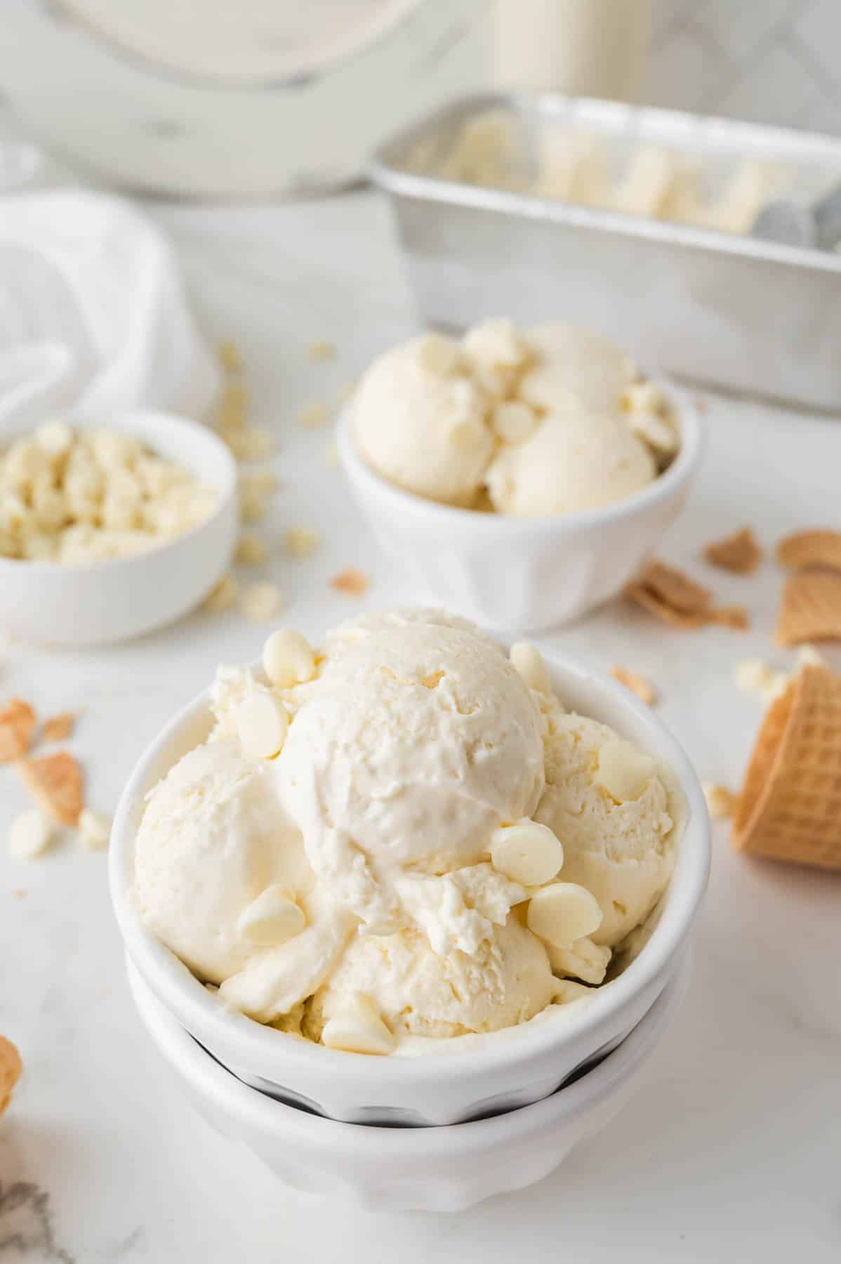 big white bowl full of white chocolate chip ice cream scoops with extra white chocolate chips