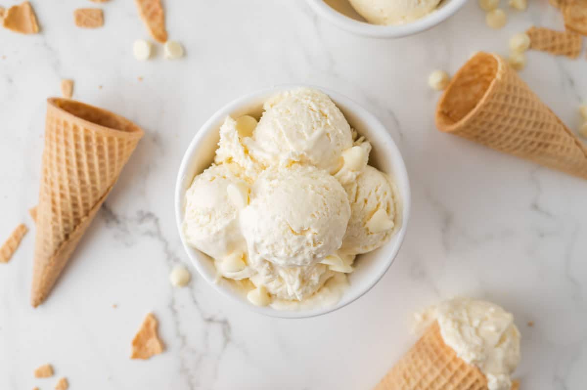 a big bowl of scoops of white chocolate chip ice cream and ice cream cones on counter