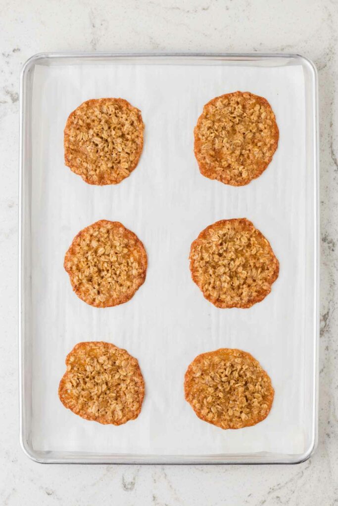 6 baked oatmeal lace cookies on parchment lined baking sheet