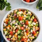 overhead shot of cucumber chickpea salad in a white bowl with a bowl of small tomatoes next to it