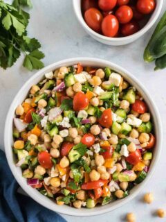 overhead shot of cucumber chickpea salad in a white bowl with a bowl of small tomatoes next to it