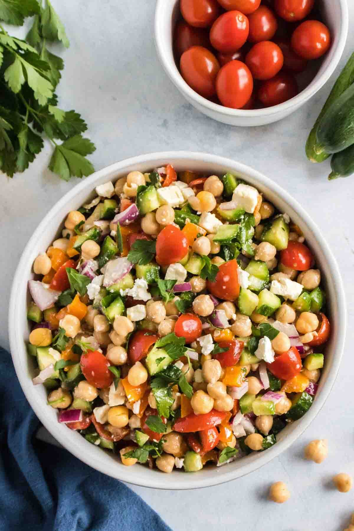 overhead shot of cucumber chickpea salad in a white bowl with a bowl of small tomatoes next to it