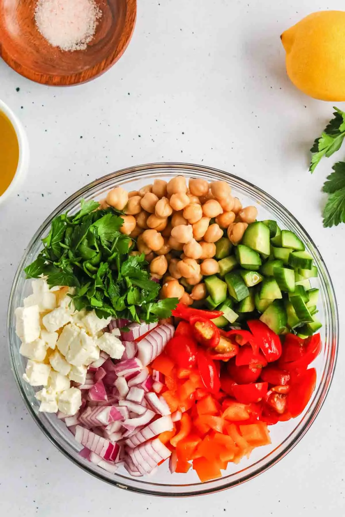 ingredients for cucumber chickpea salad arranged in a clear mixing bowl (before mixing together)