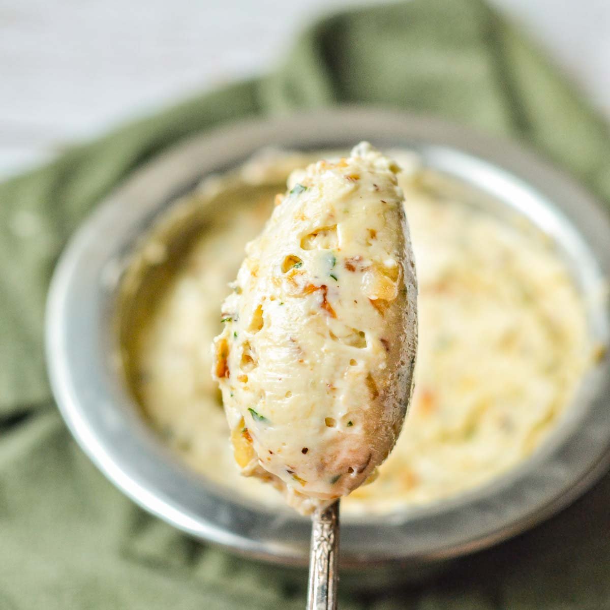 close-up picture of a spoonful of French onion compound butter, with the full bowl of butter in the background with a green kitchen towel