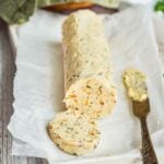 roll of French onion compound butter with a slab cut off the front, with the butter knife laying next to it