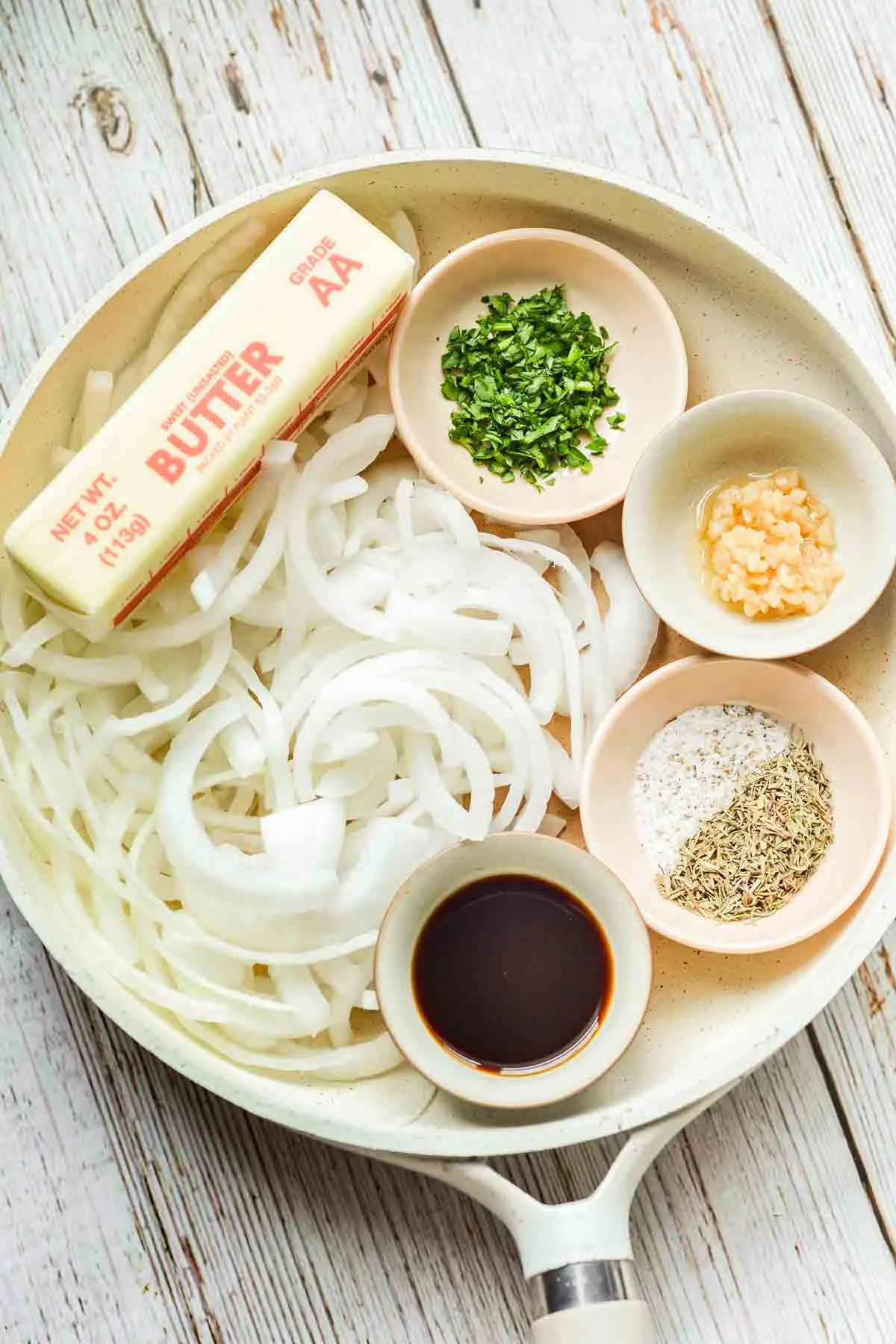 ingredients for compound butter in separate bowls on a plate, with sliced onions and a stick of butter