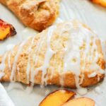 a peach scone with drizzled glaze with a few fresh peach slices laying next to it