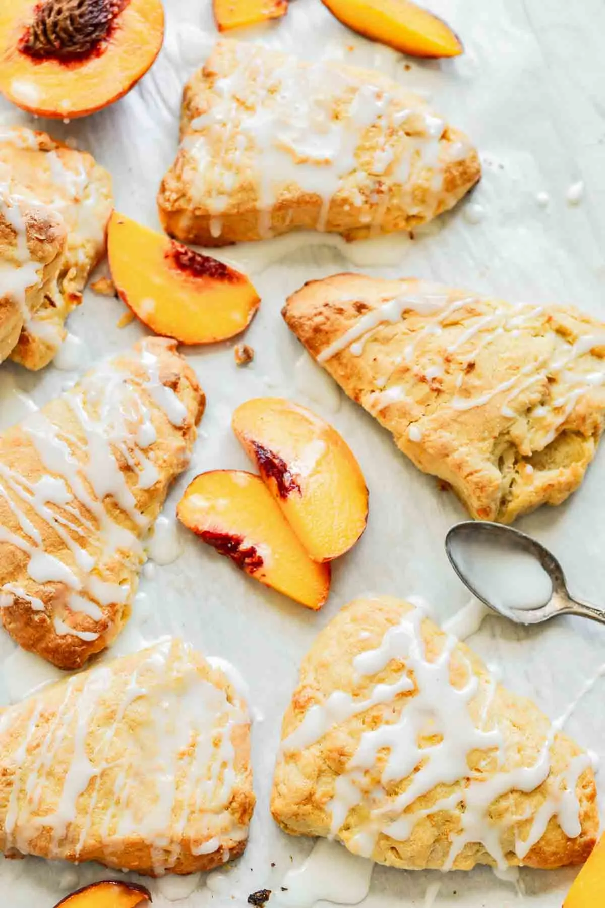 several peach scones with fresh peach slices and a spoon with glaze drizzle