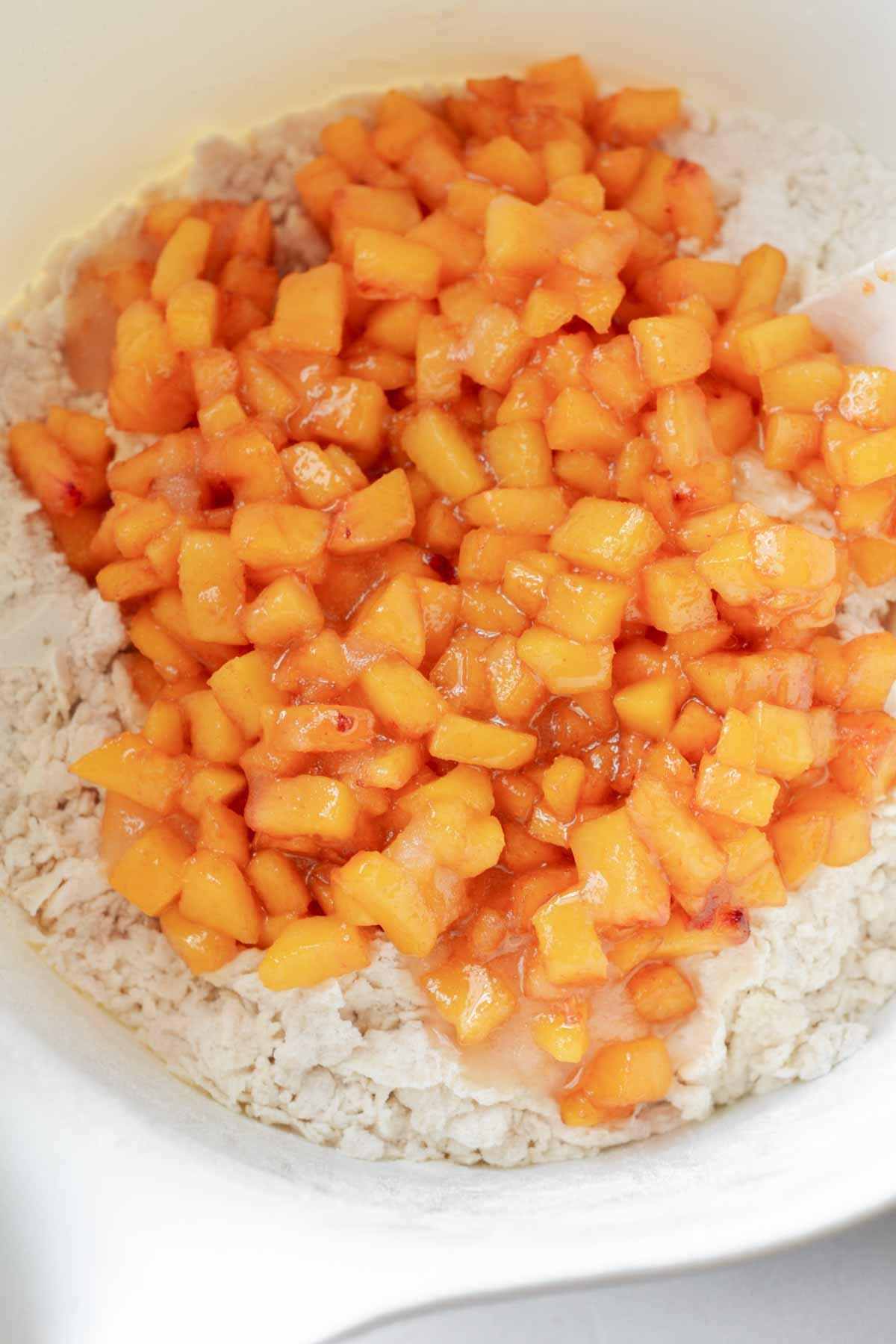 fresh peach chunks on on top of dry scone ingredients in white mixing bowl