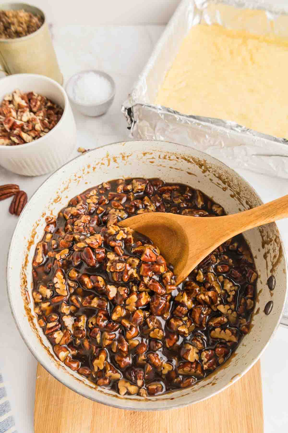 a mixing bowl with pecan pie bar filling, being stirred by a wooden spoon